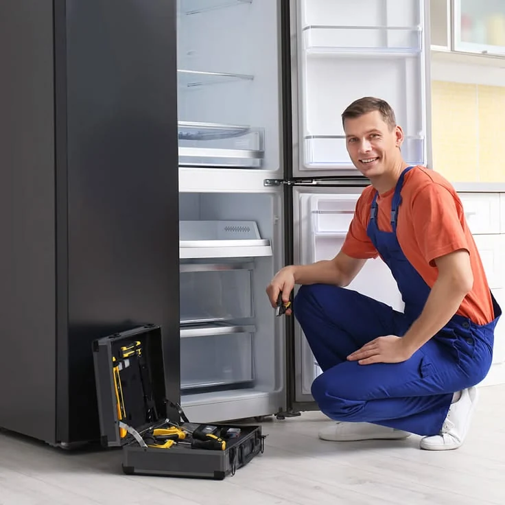 Technician kneeling beside an open refrigerator with a service toolbox